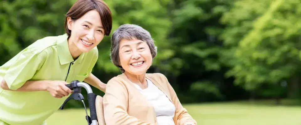 車椅子で散歩中の笑顔の高齢女性と介護スタッフ
