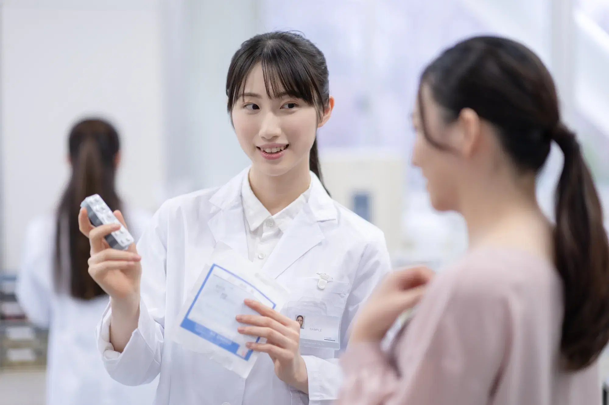 髪を結んだ薬剤師が女性に薬の説明をしている