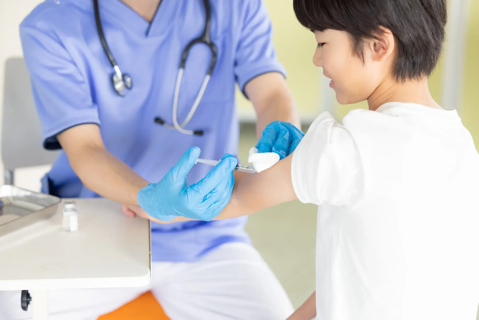 首から聴診器を下げている人間が子どもの左腕に薬液を注射