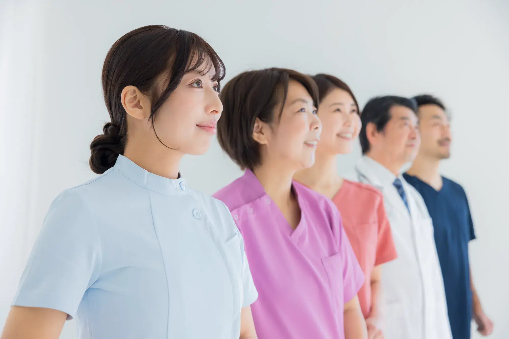 奥に向かってそれぞれ別の色の服を着た医療従事者の人が並んで立っている