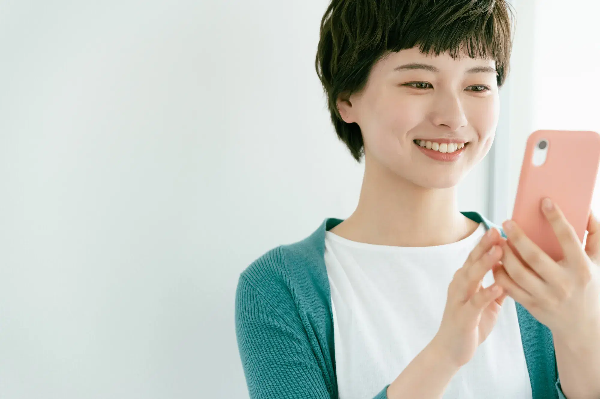 緑色のカーディガンと白い服を着た女性が、スマートフォンを操作している。