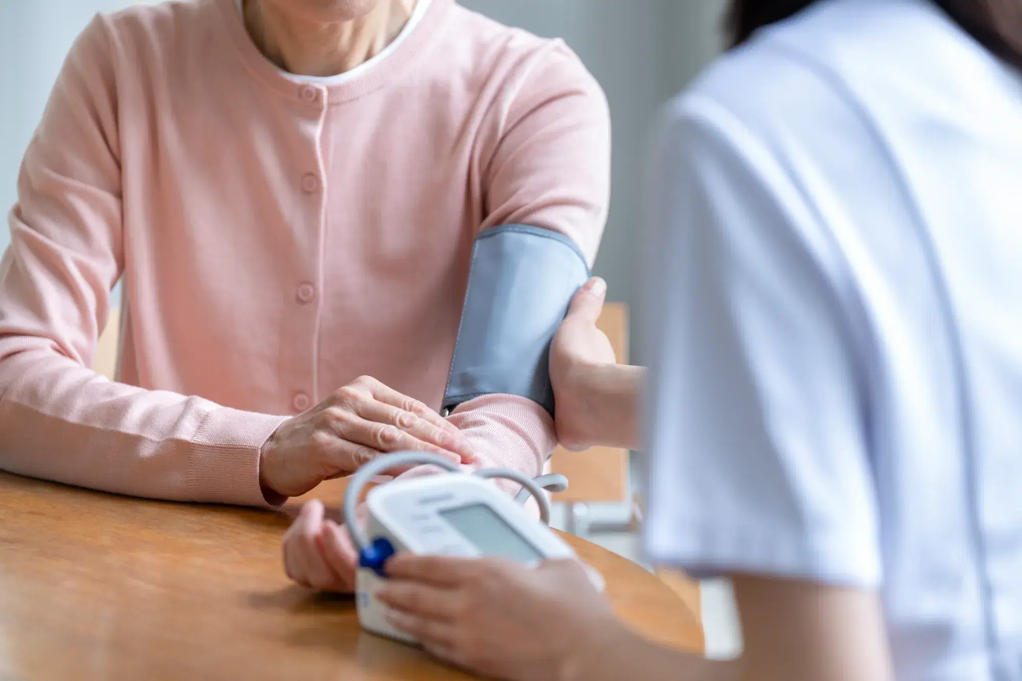 ピンク色の服を着た人間の左腕から血圧測定を行う白い服を着た人間