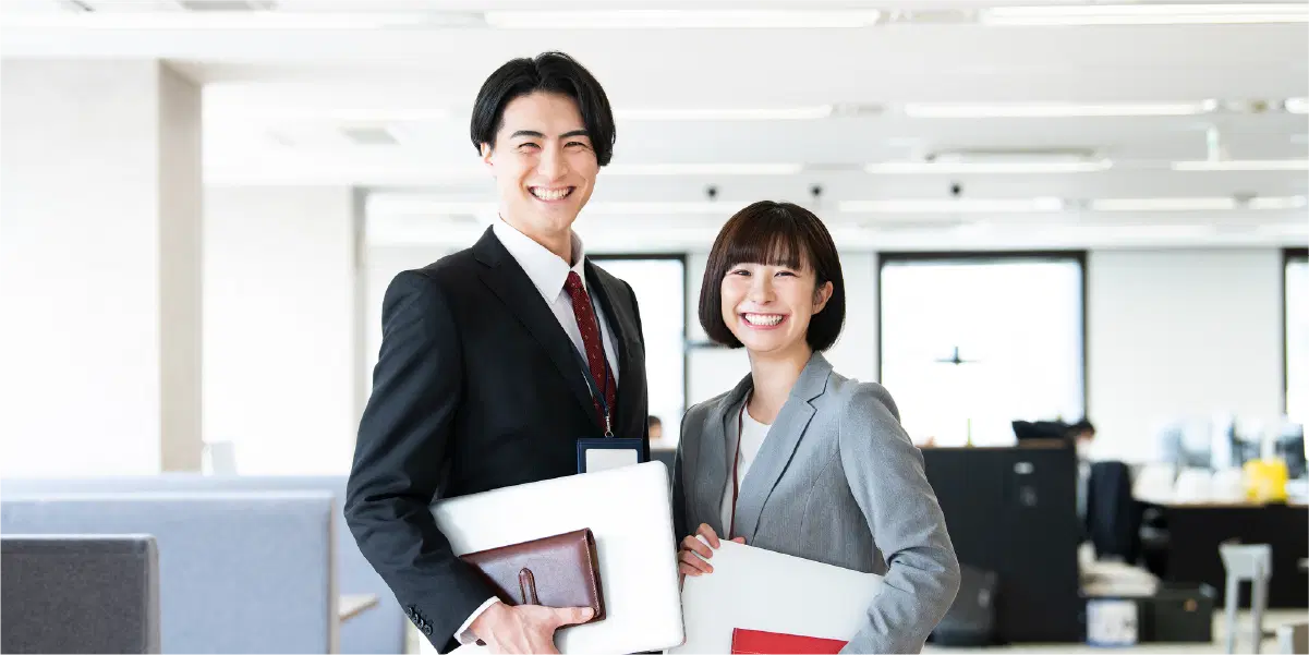 メモ帳とPCを持ち笑っている男女