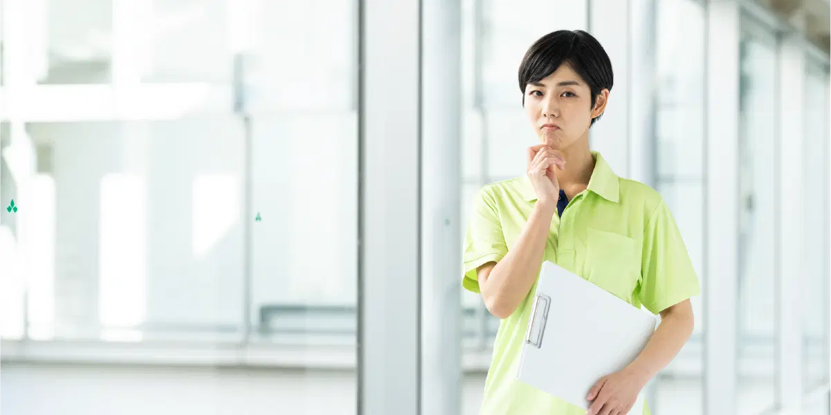 黄色い服を着た男性がバインダーを持ち廊下を歩きながら考え事をしている