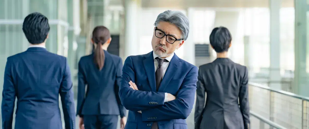 背景に背を向けているスーツ3人とこちらを向いて難しく考え込んでるスーツの男性