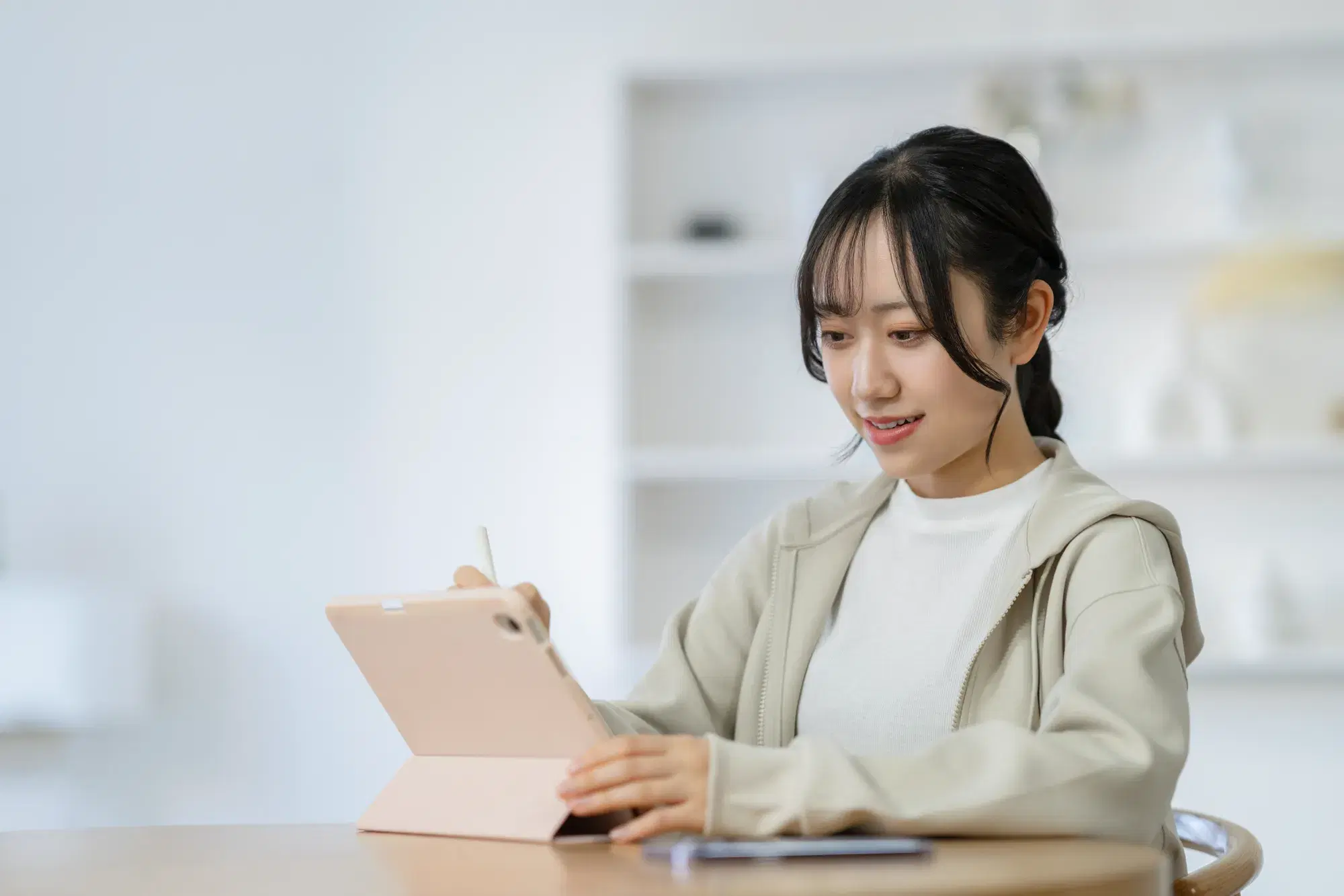 ピンク色のタブレット端末を操作するベージュ色のパーカを着た女性