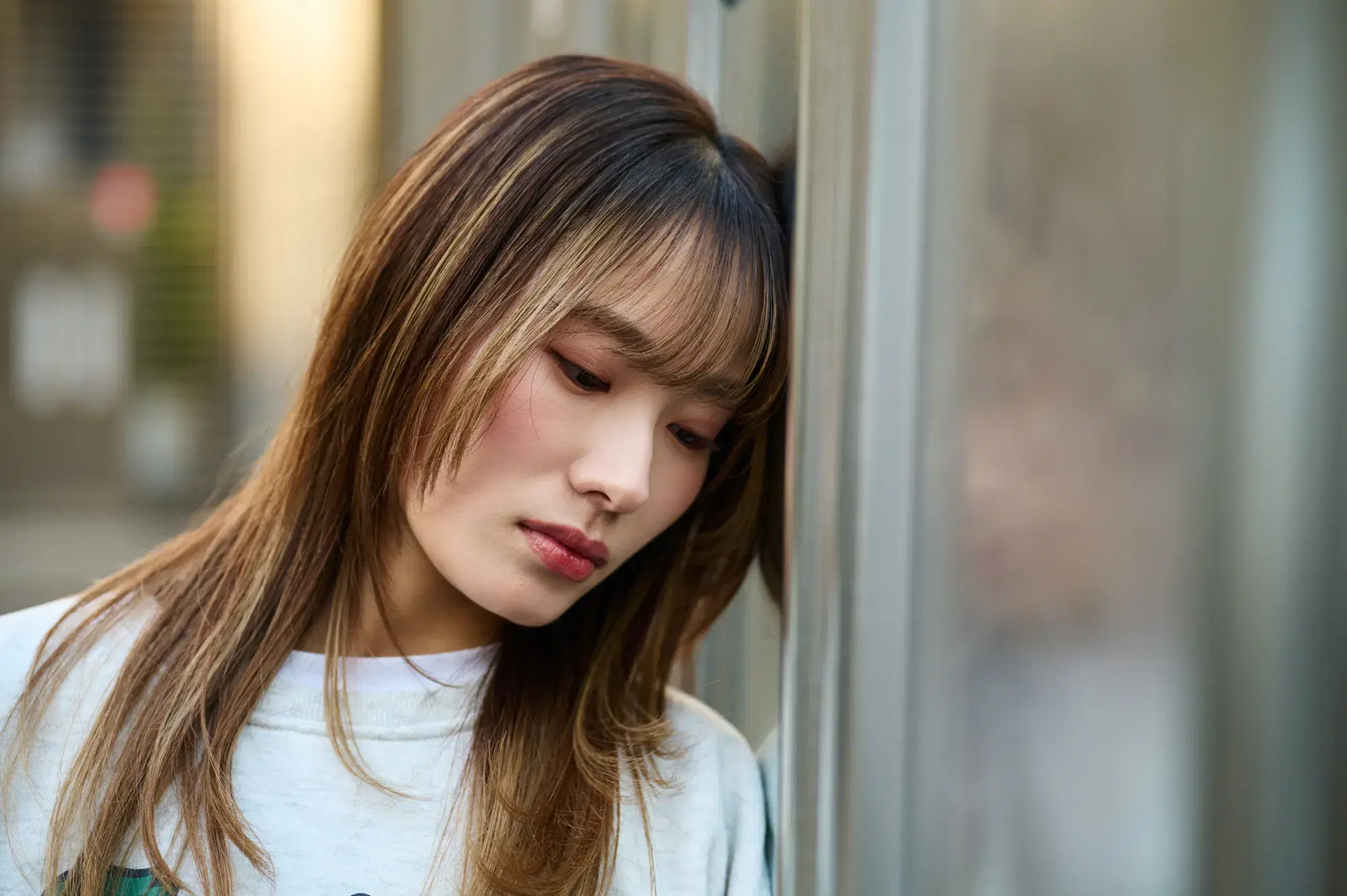 白い服を着た女性が頭を壁つけてもたれかかっている