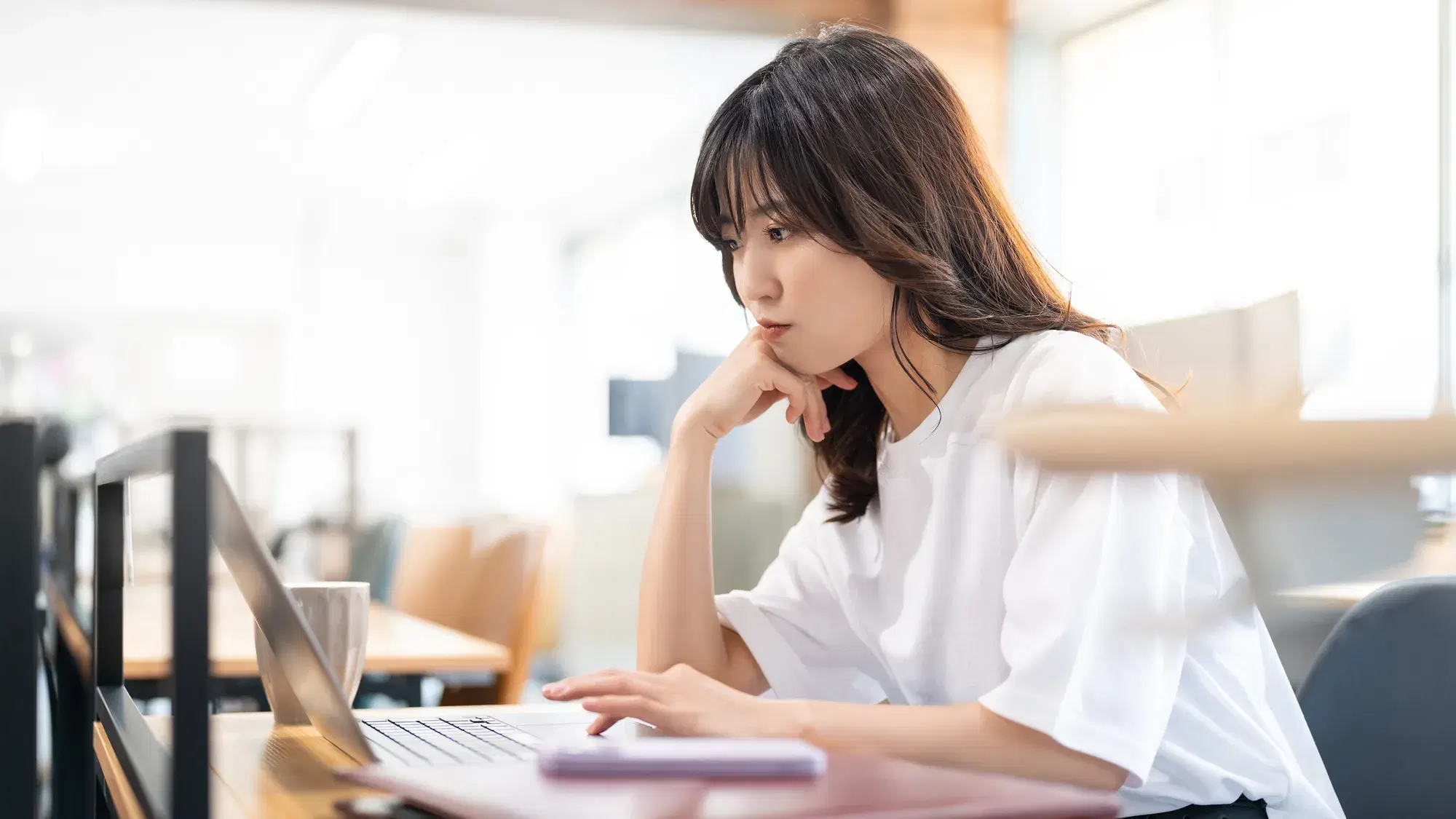 カフェの店内で頬杖をついているパソコンを見ている白い服を着た女性