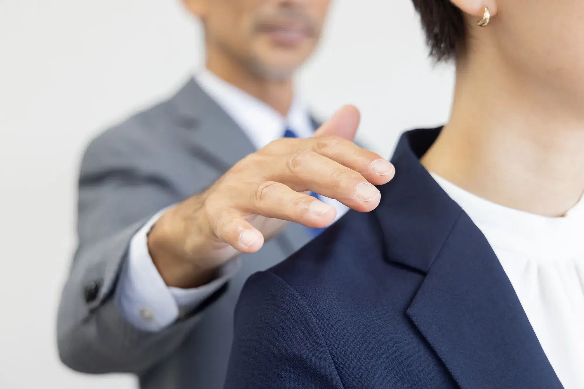 灰色のスーツを着た男性が社員の女性の肩に触れようとする瞬間