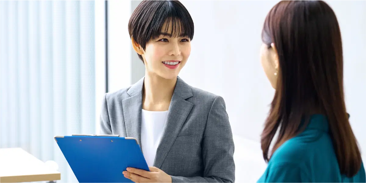 青いバインダーを持ち笑顔で話を聞くショートカットの女性