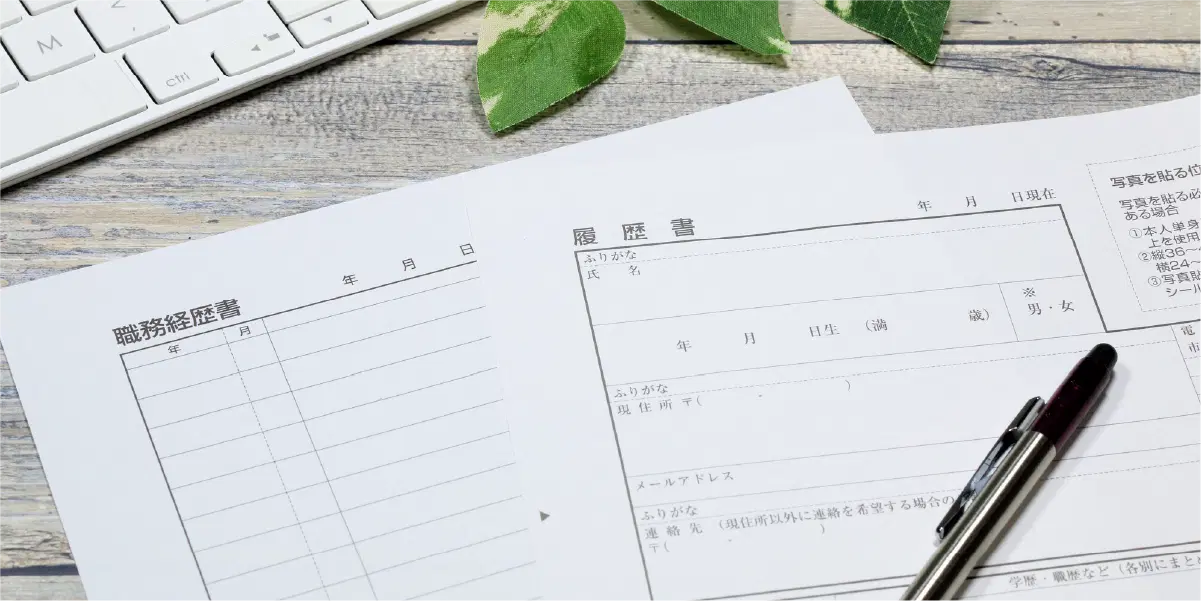 履歴書の上に黒いペンが置かれ、葉っぱとキーボードが見切れている