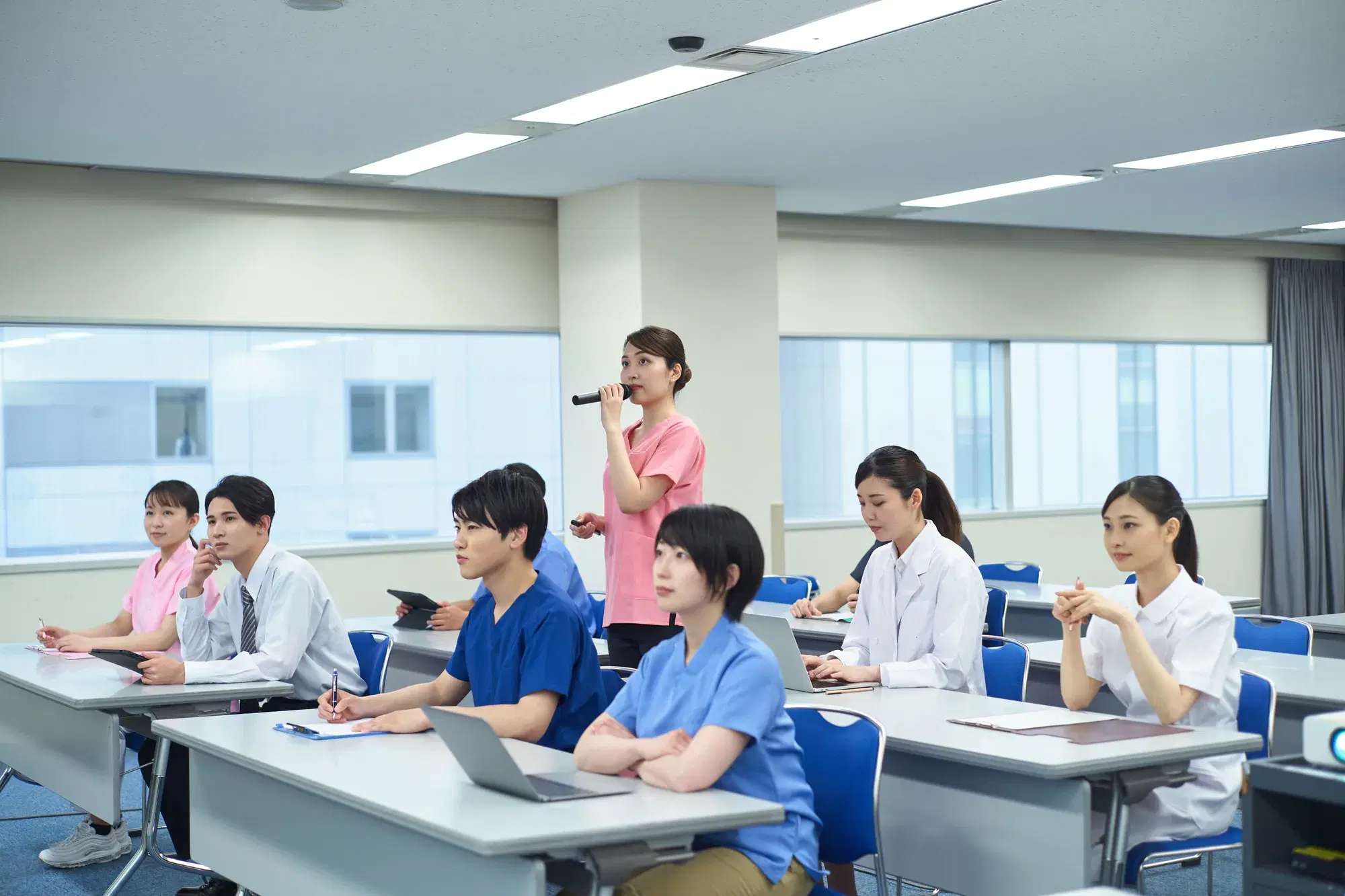 医療関係の集会でピンクの服を着た女性がマイクを持って発言