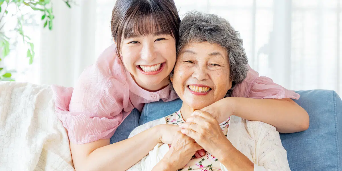 ピンクの服を着た女性が年配の女性に後ろから抱きついている