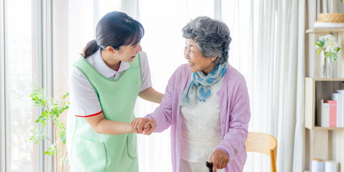 杖をついた老人の手を掴み微笑む職員
