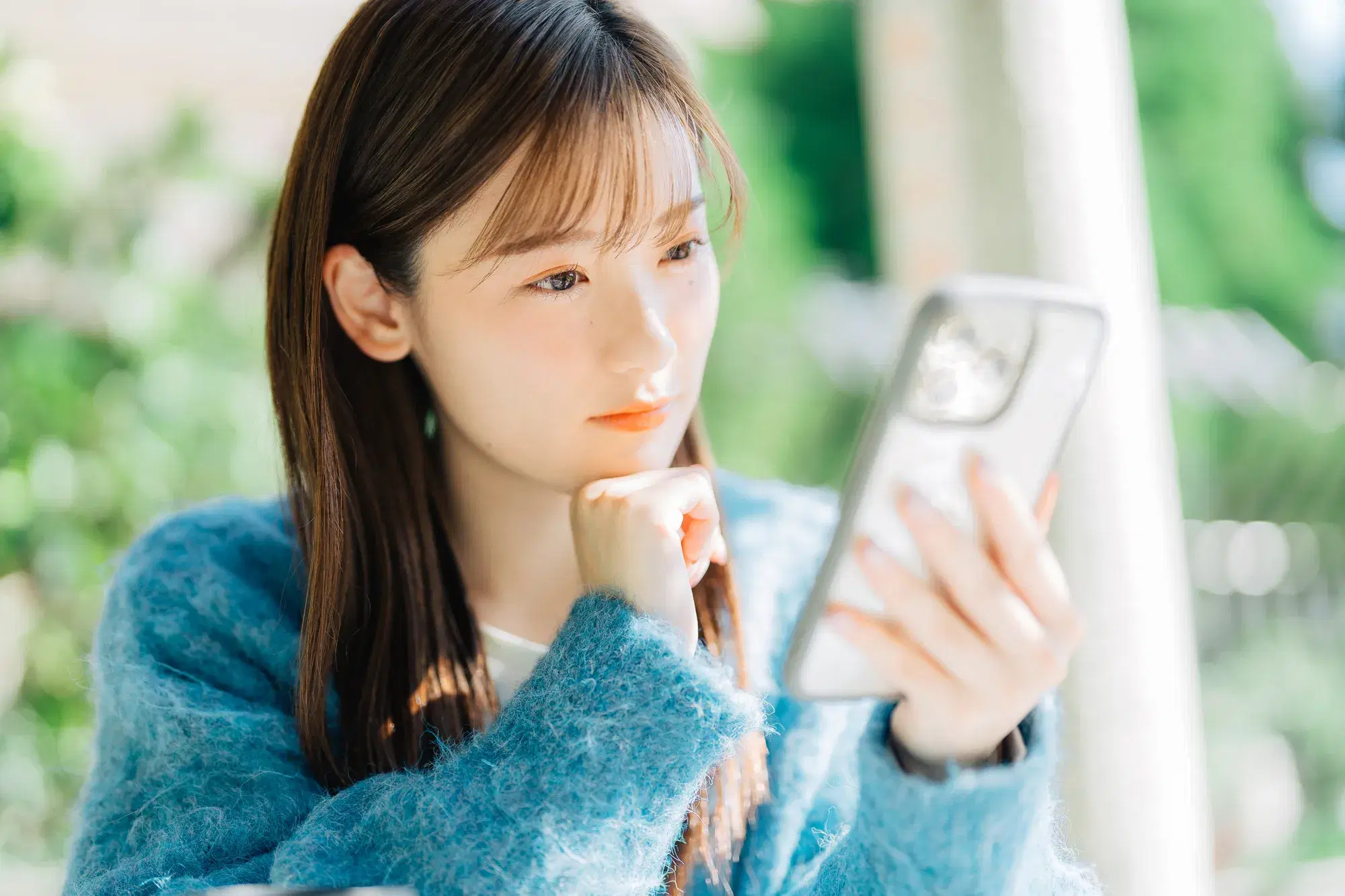 白い色のスマホを操作している水色の服を着た女性