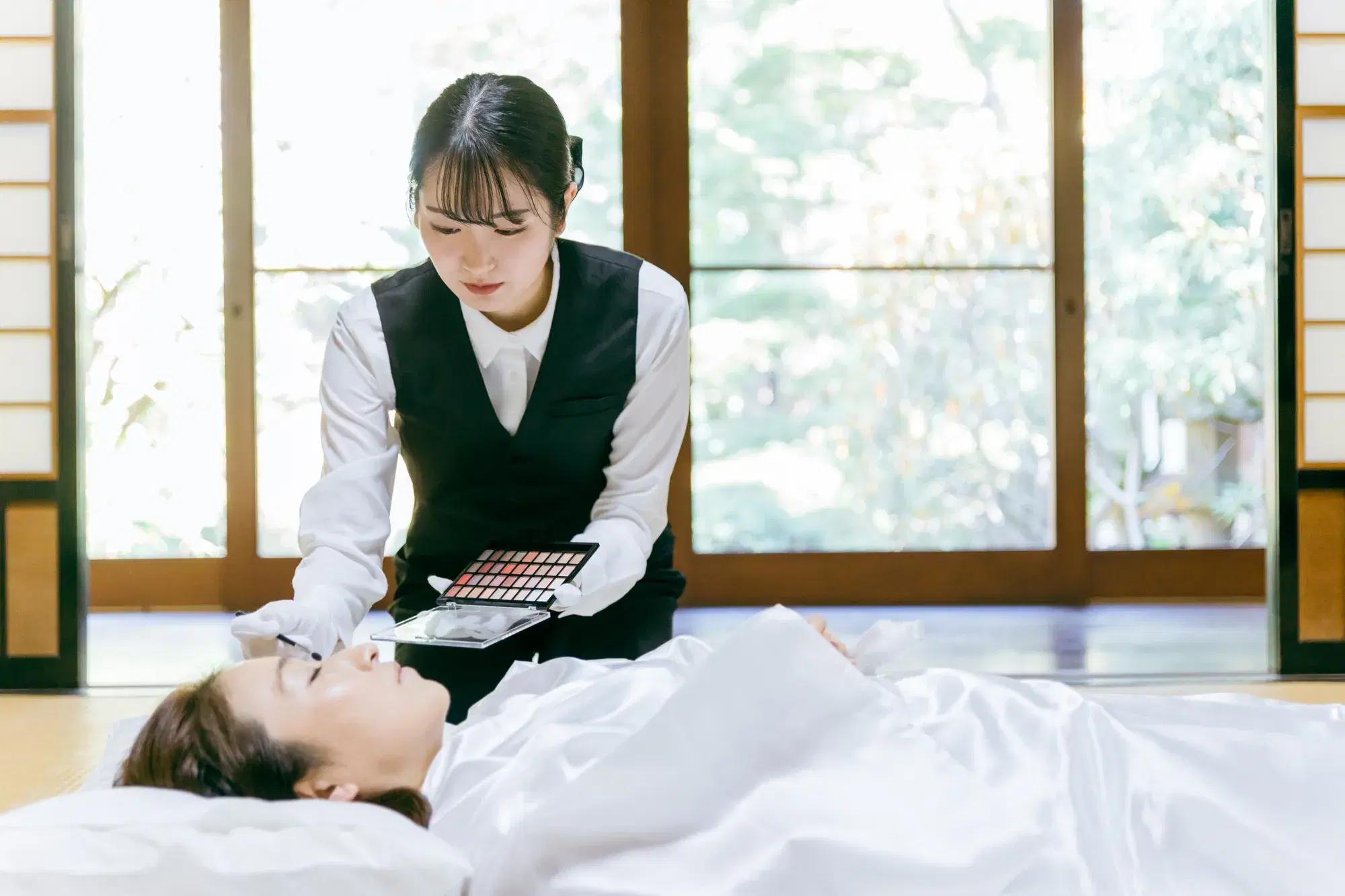 葬儀屋の女性が遺体に化粧を施している。