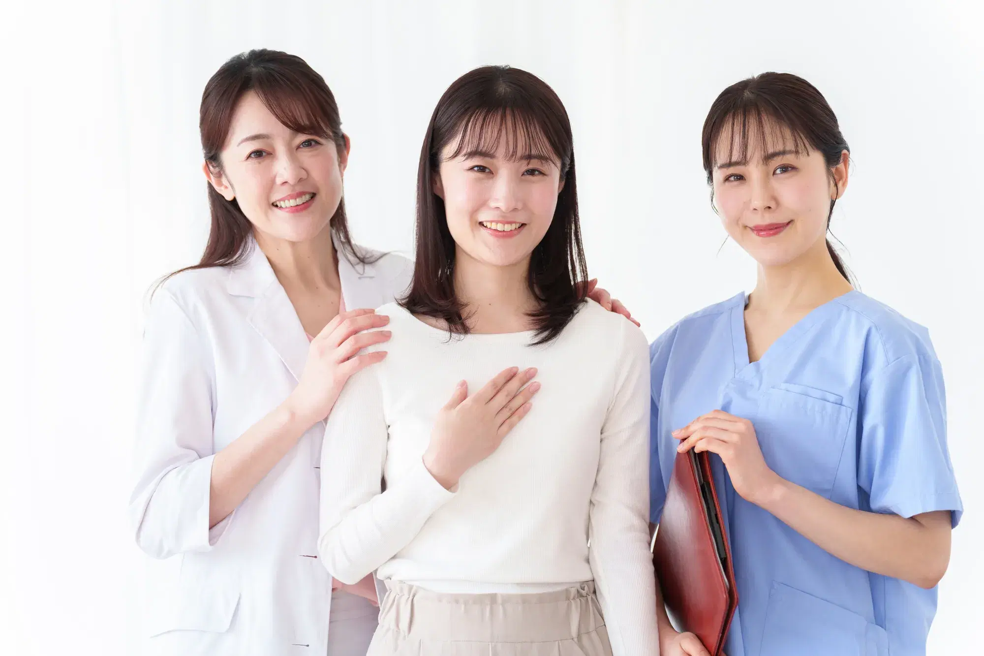 左から白衣を着た女医と、白いふうにベージュのスカートを履いており、胸に手を当てている女性と、バインダーを持った青い服を着ている医療従事者の女性がいる。