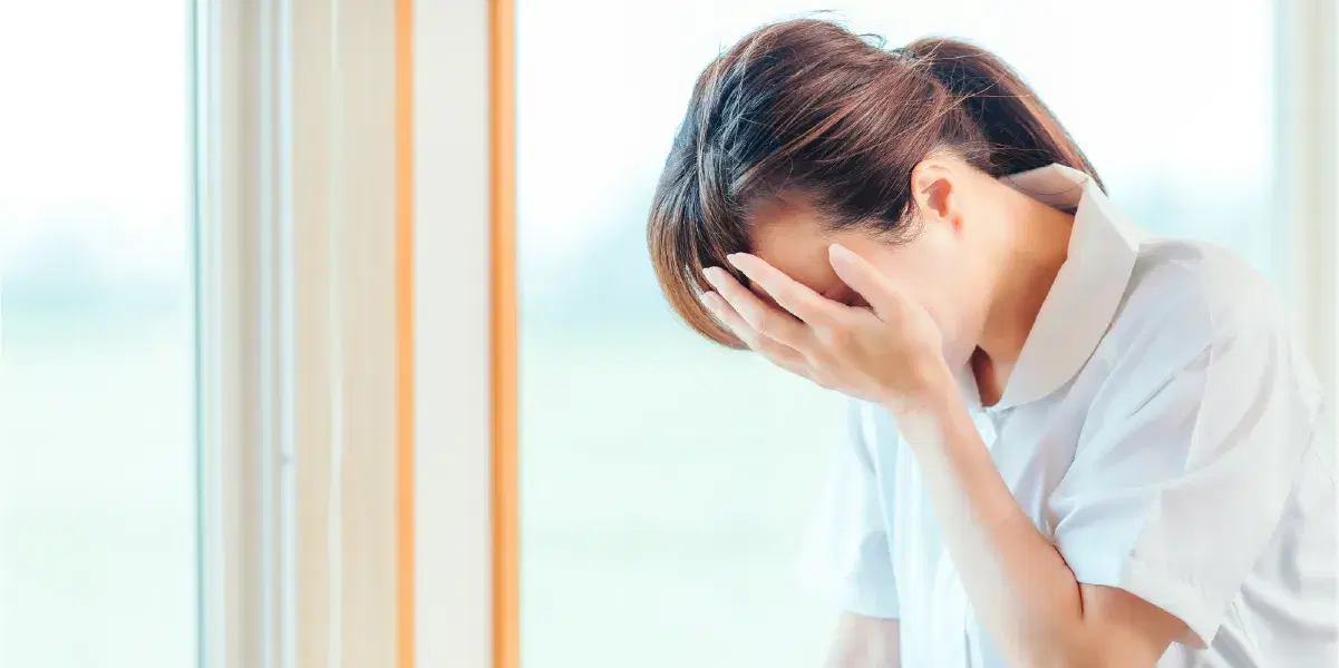 頭を抱えて辛そうに壁に寄りかかる看護職員女性