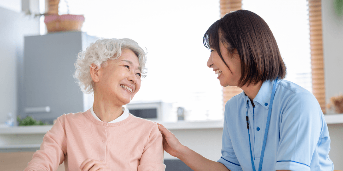 青い服を着た女性が年配の女性の肩に触れている