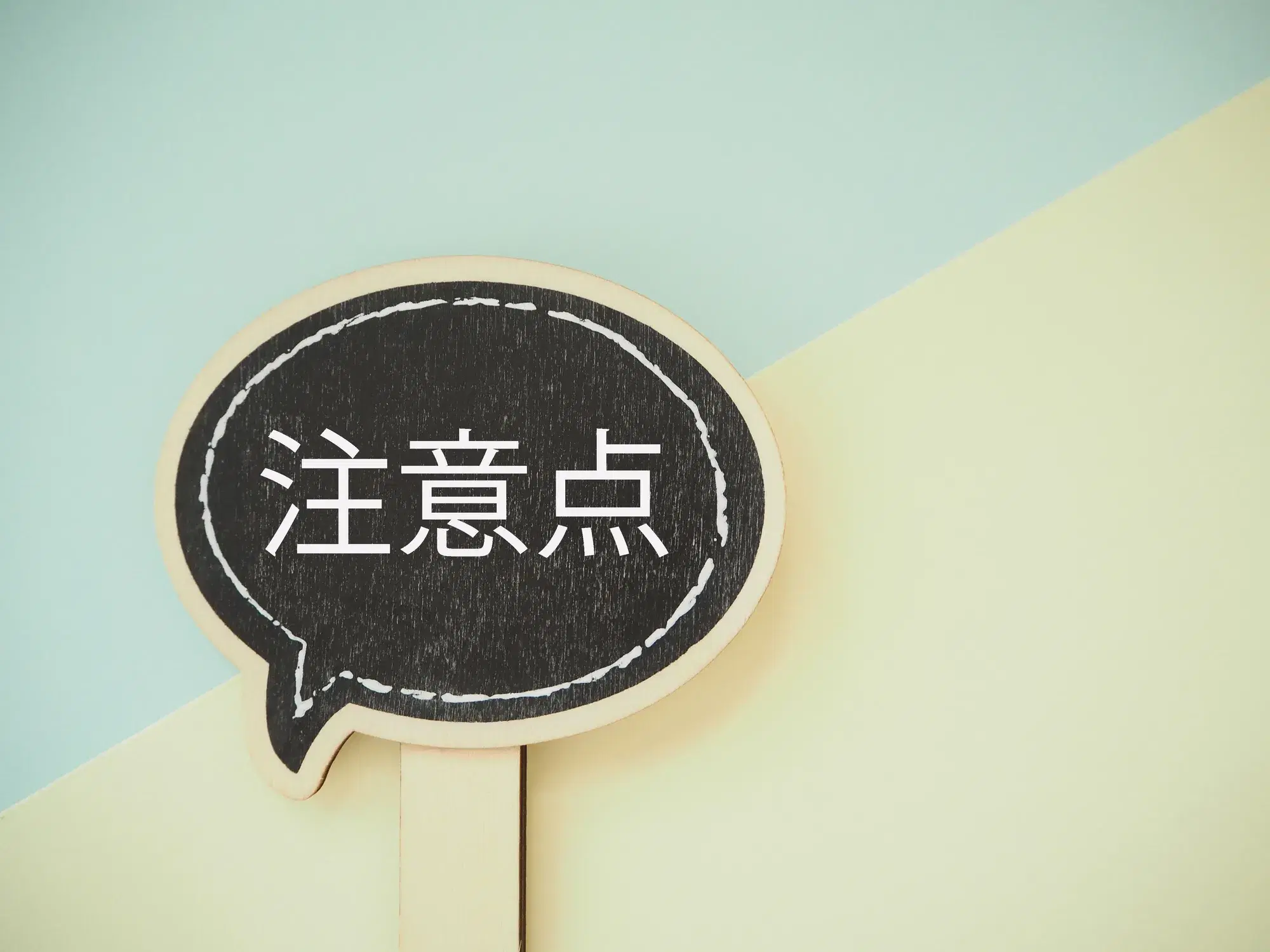 水色と黄色の背景に注意点と白い文字で書かれた黒い木製の吹き出しが置いてある。