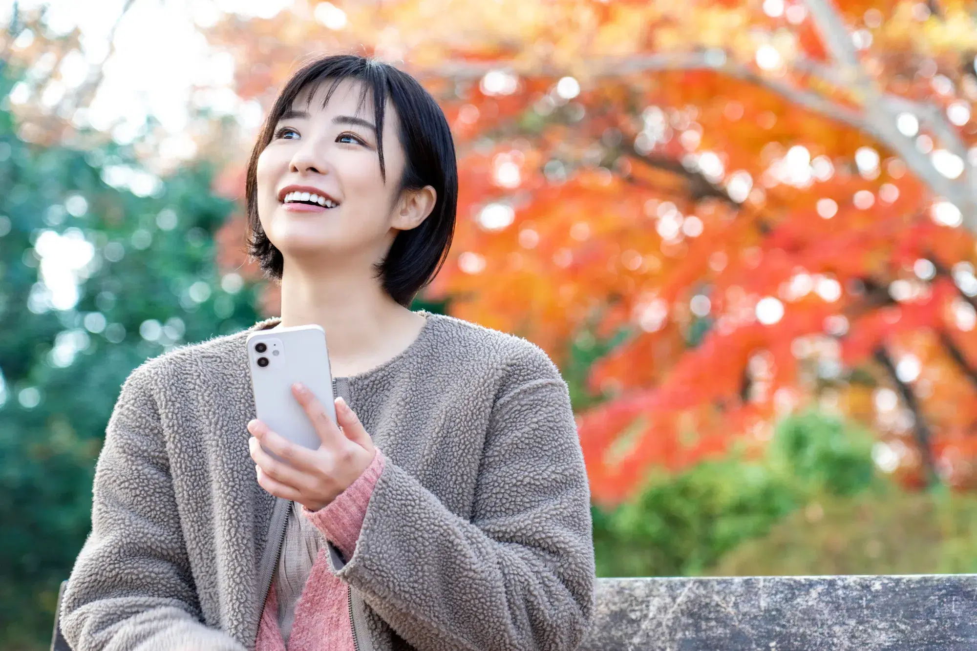 グレーの服を着た女性がスマートフォンを持って空を見上げている。