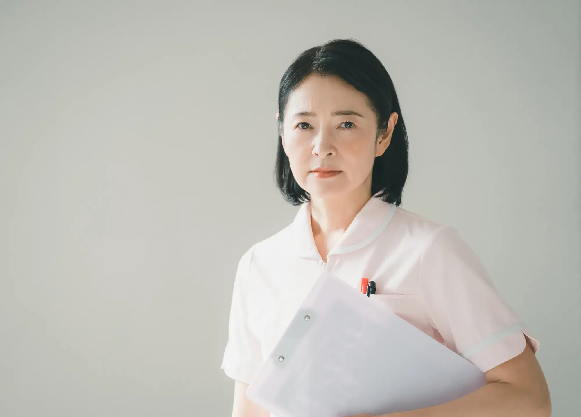 薄いピンク色の服を着た女性が白いバインダーを抱えてこちらを見つめる