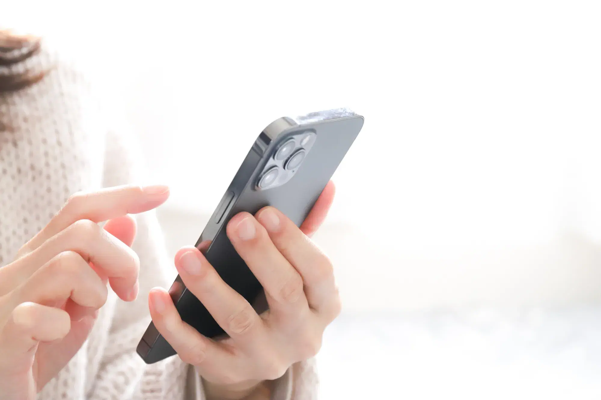 白いセーターを着た人がスマホを左手に持ちながら操作