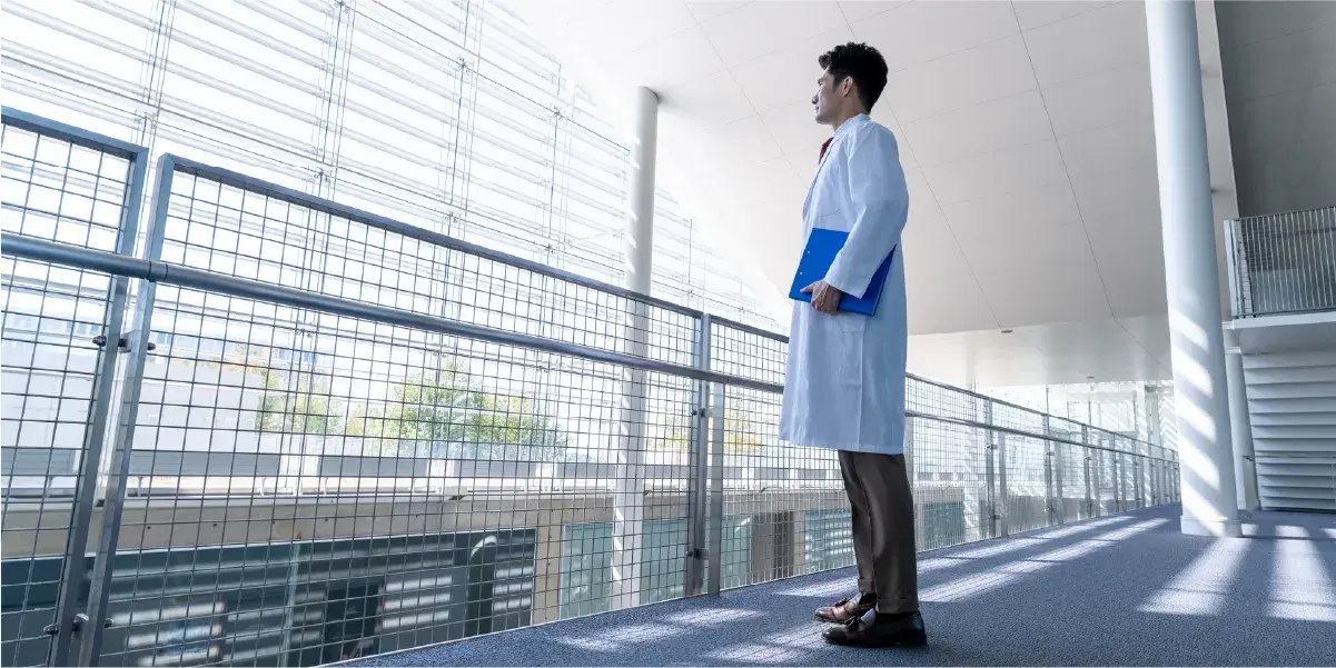 窓の外を眺めるバインダーを持った白衣の男性