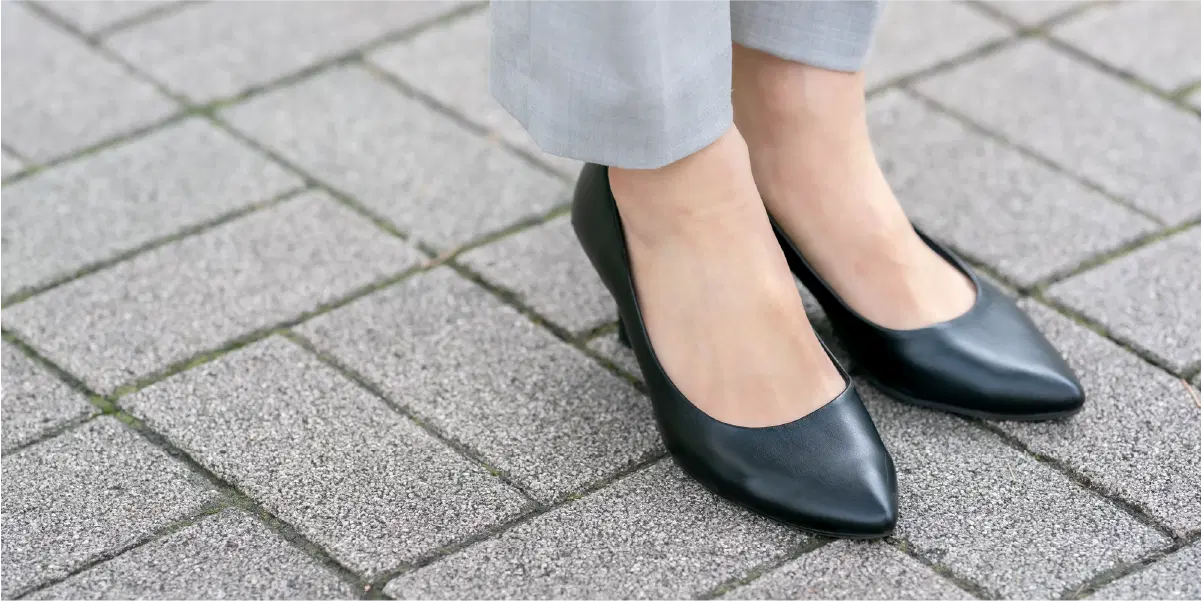 グレーのパンツと黒いヒールを履いた女性の足元