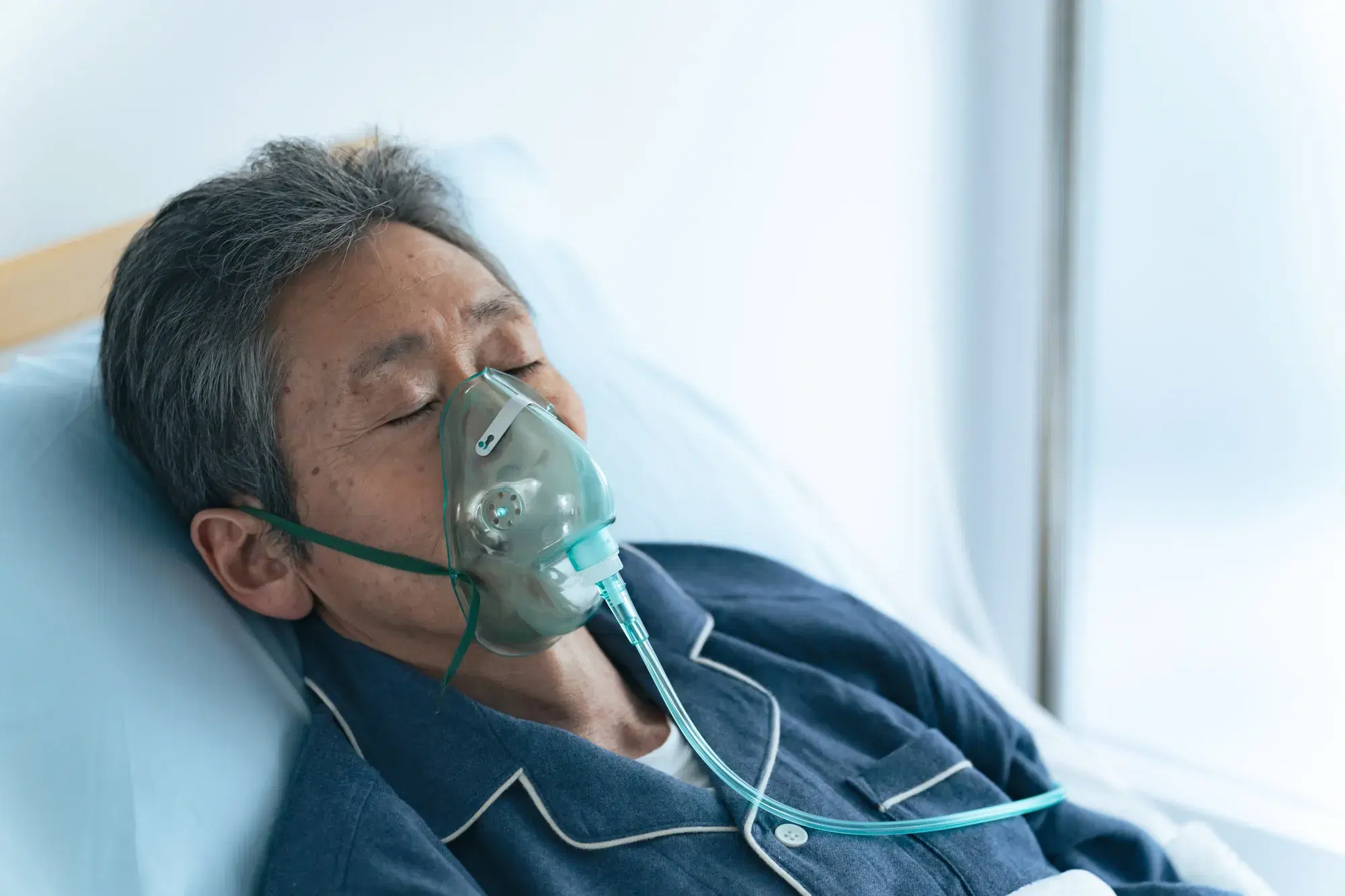 高齢の男性が酸素マスクを着用しベッドに寝ている