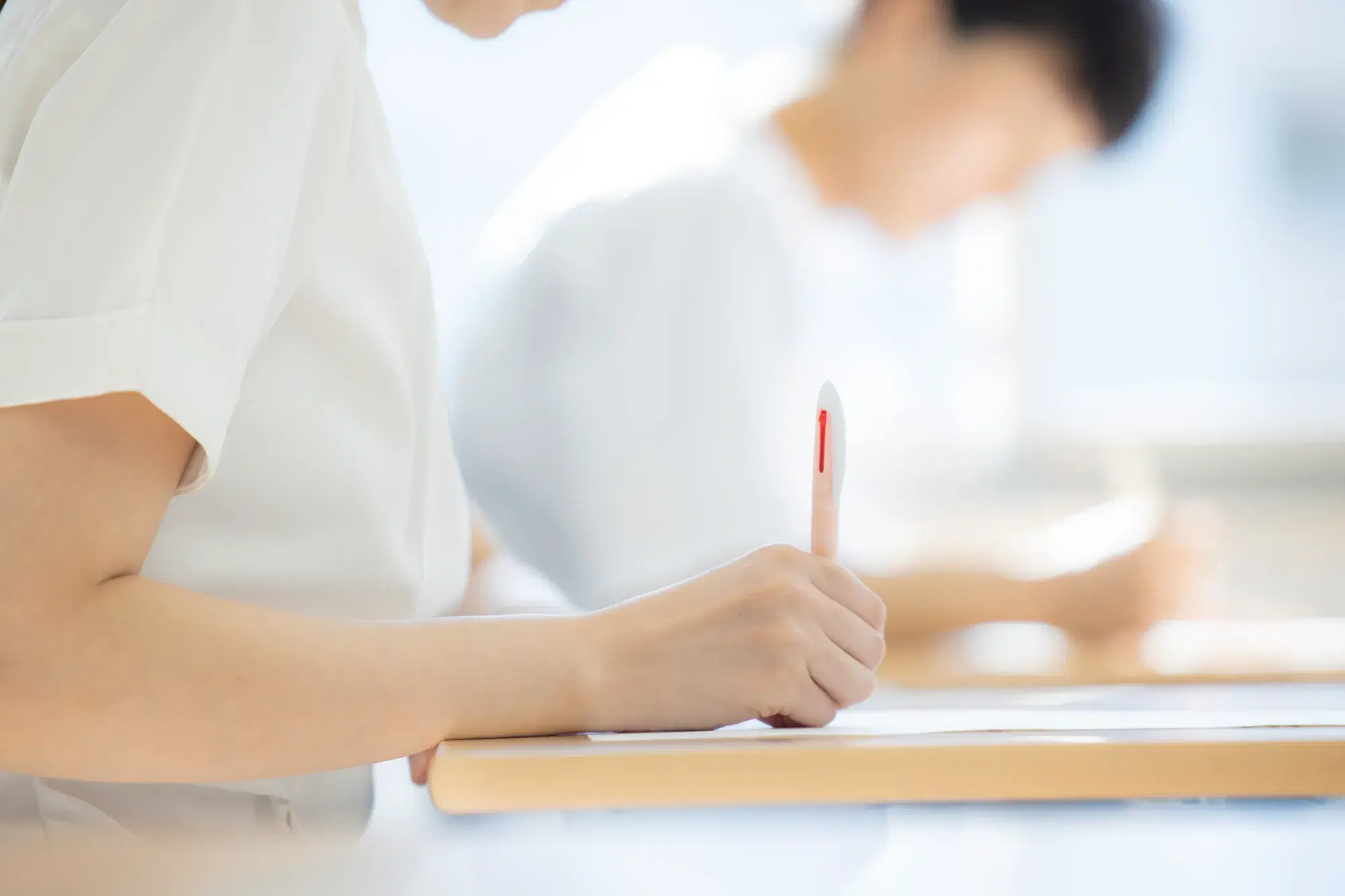白衣を着ているであろう女性がピンクのペンで紙に文字を記している