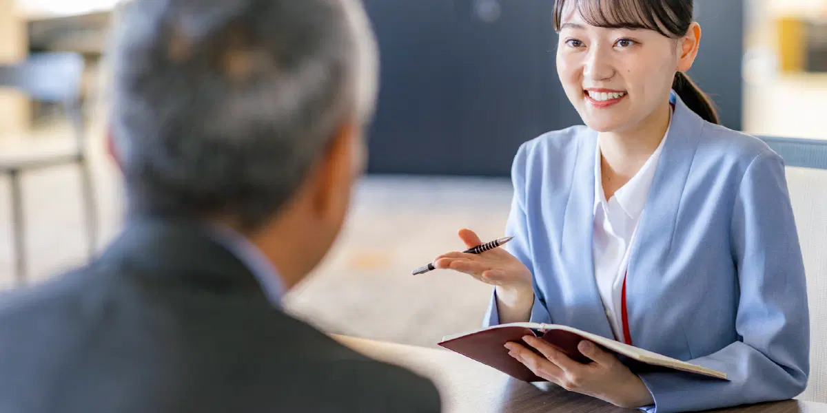 ペンを持っている若い女性が年配の男性に説明している