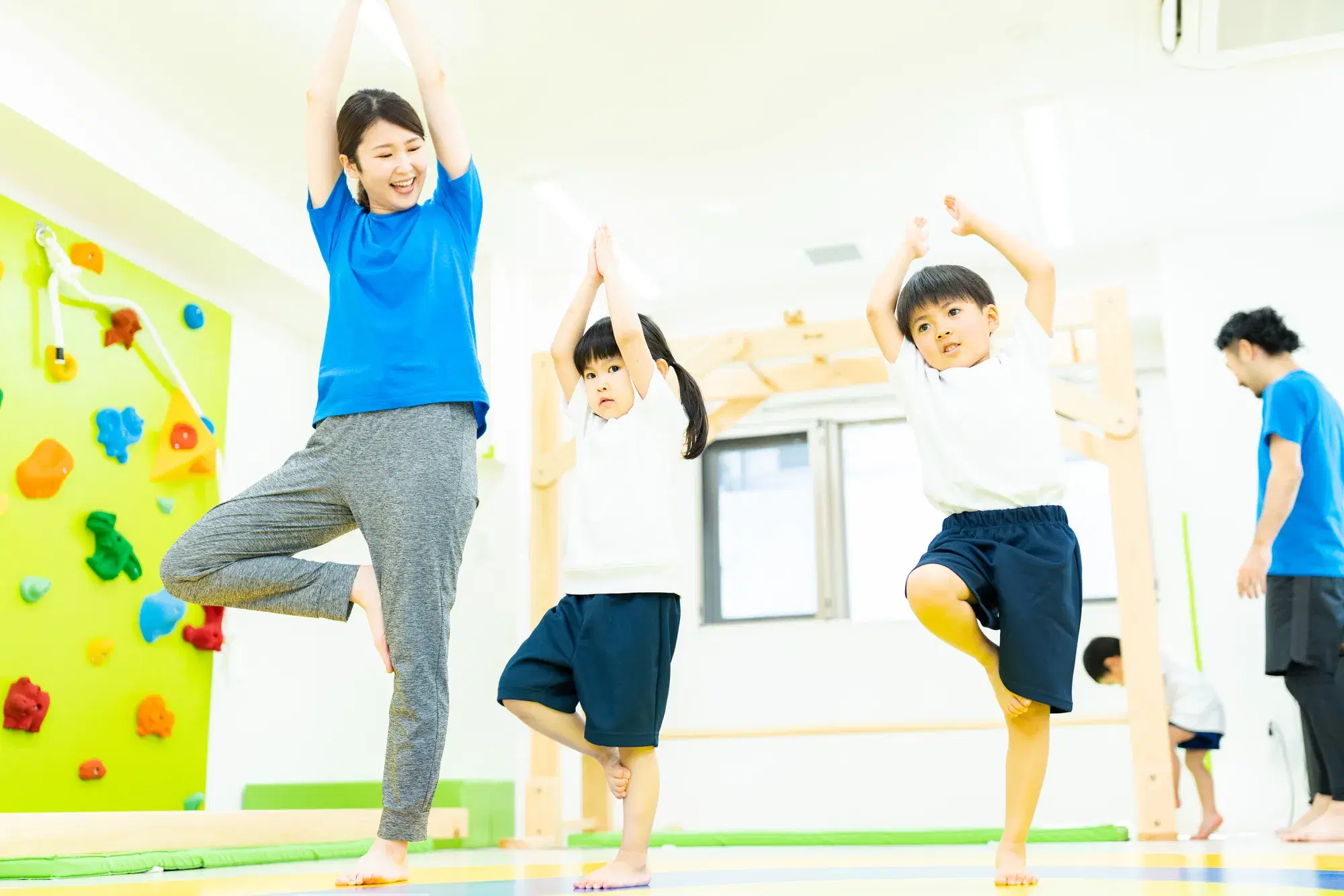 体操服を着た子供が水色の服を着た先生と一緒に体操をしている