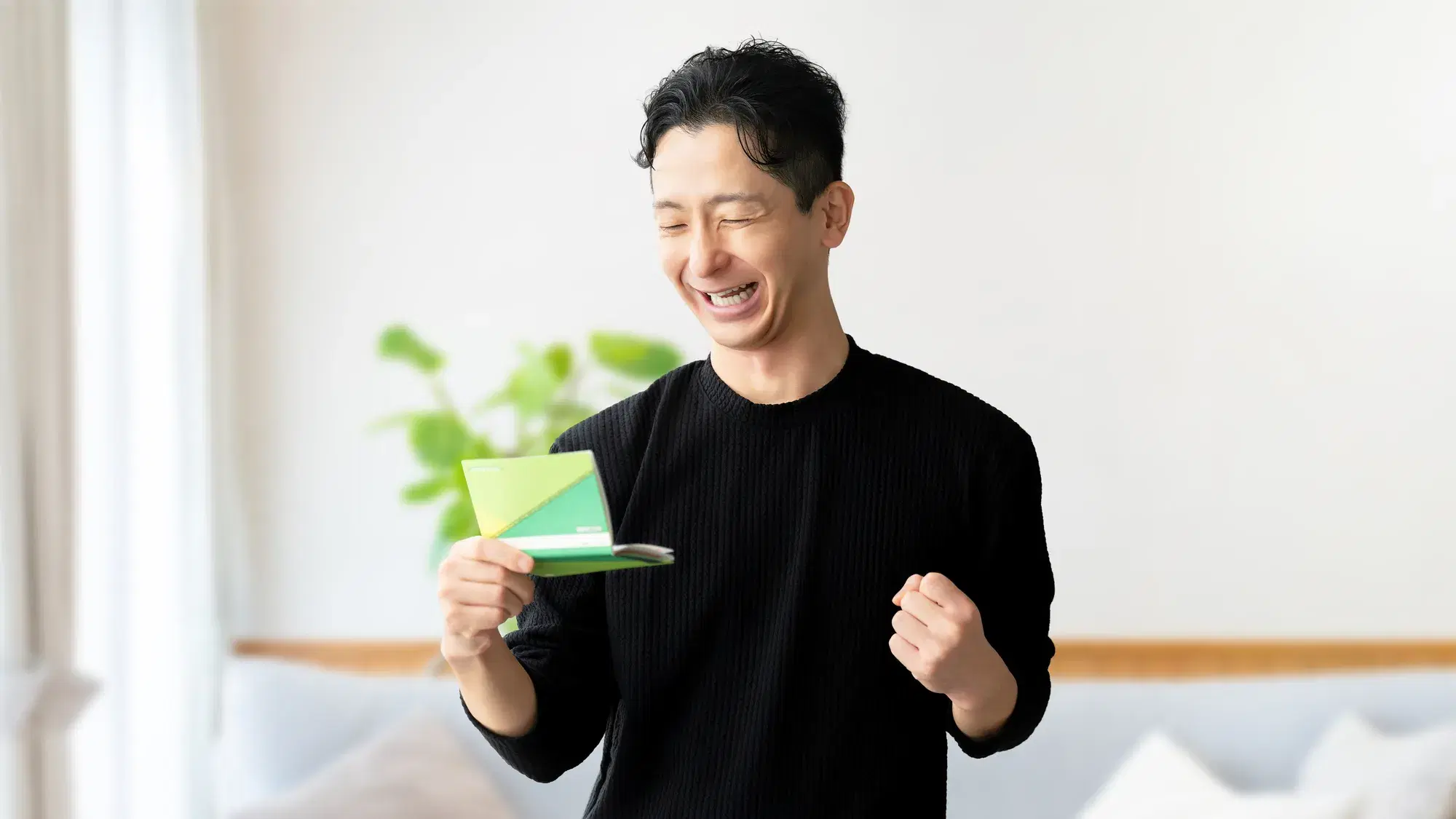 黒い服を着た男性が通帳を右手にガッツポーズ
