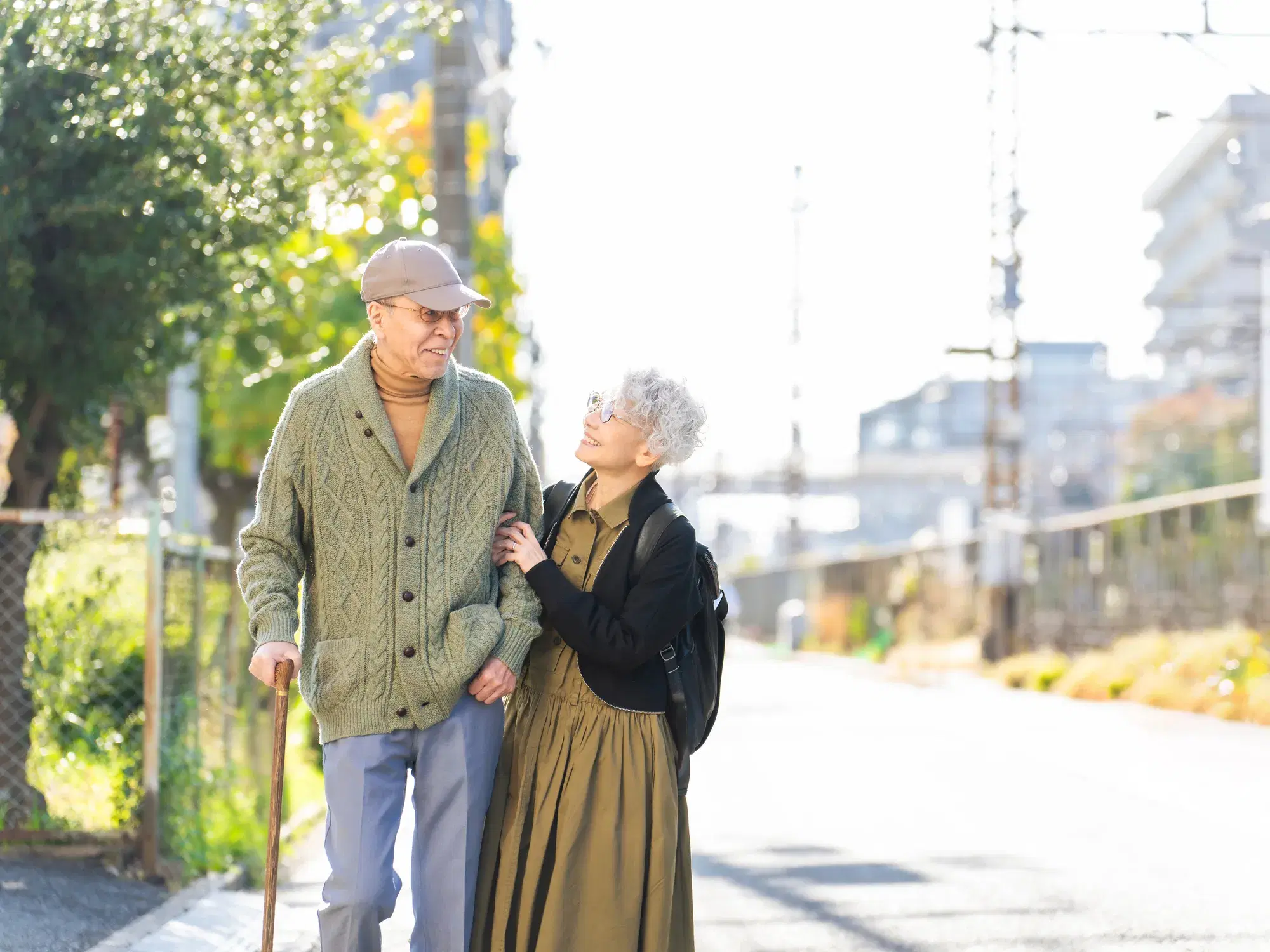 薄緑色の服を着た杖を突いて歩く年配の男性と黒色の上着を着た年配の女性