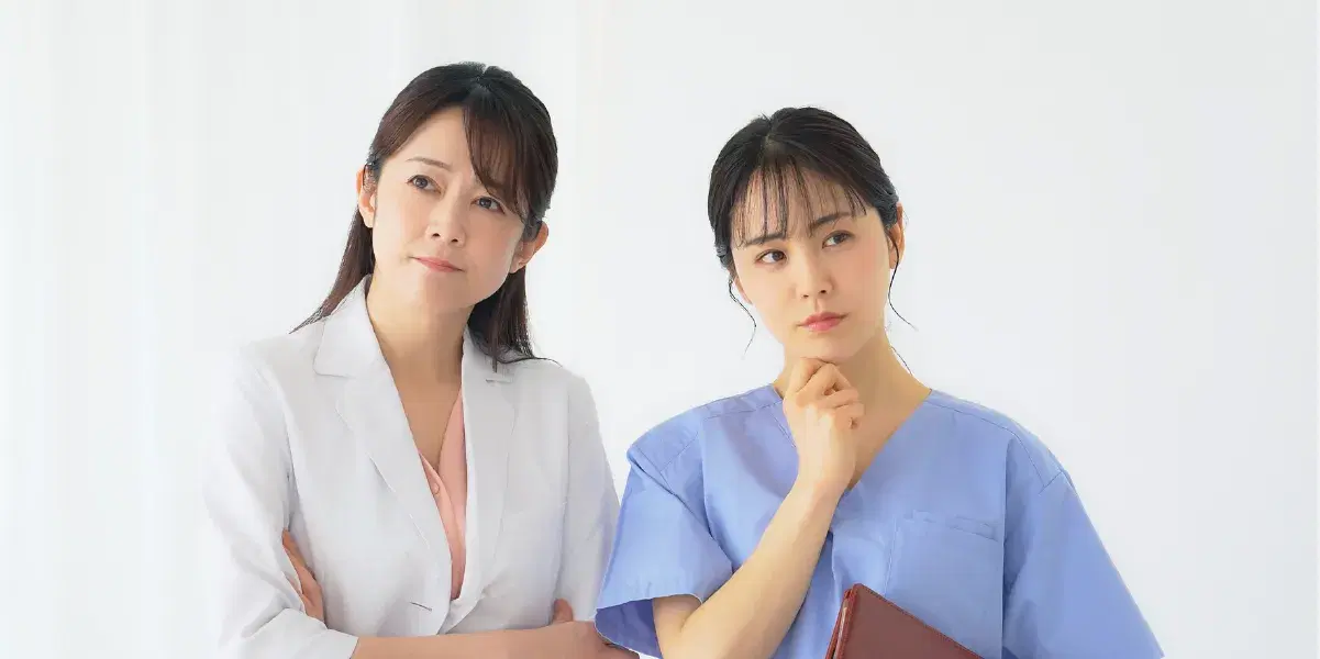 首を傾げ考える様子のバインダーを持った医療職員の女性たち