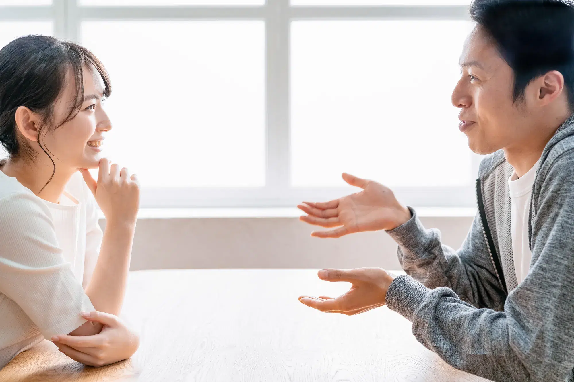机を挟んで話し合っている白い服を着た女性と灰色の服を着た男性