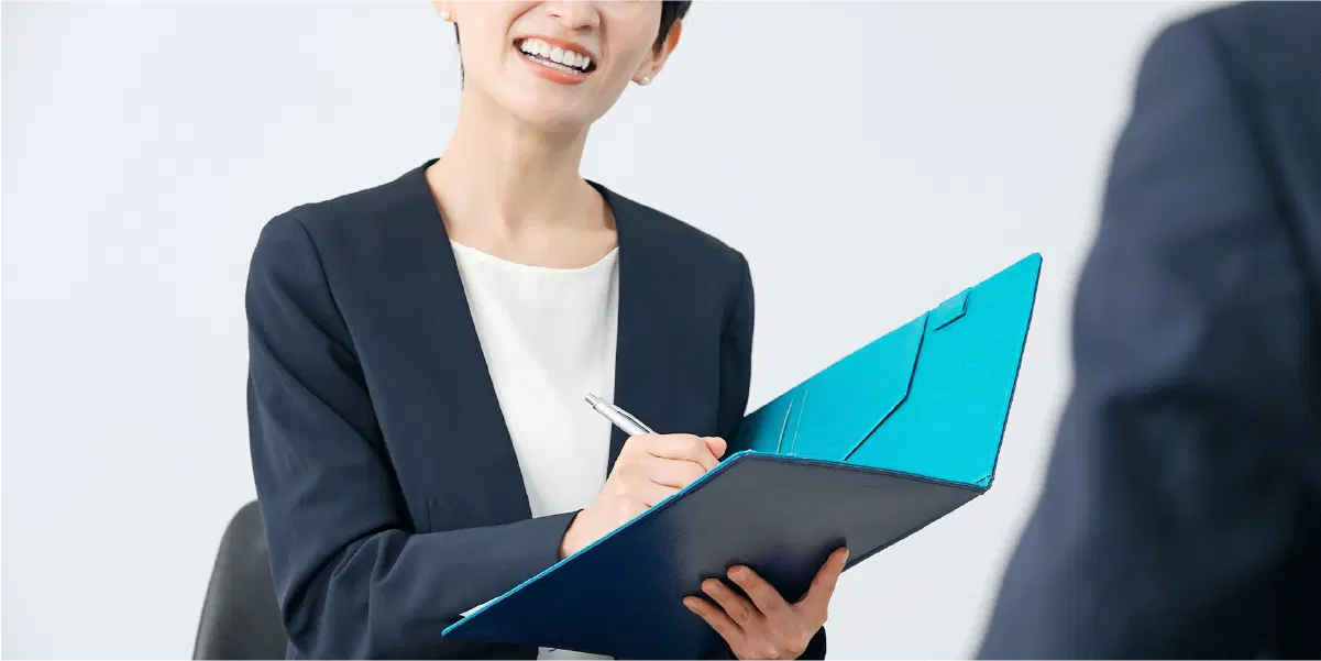 話を聞きながらペンでバインダーに何かを記入する女性