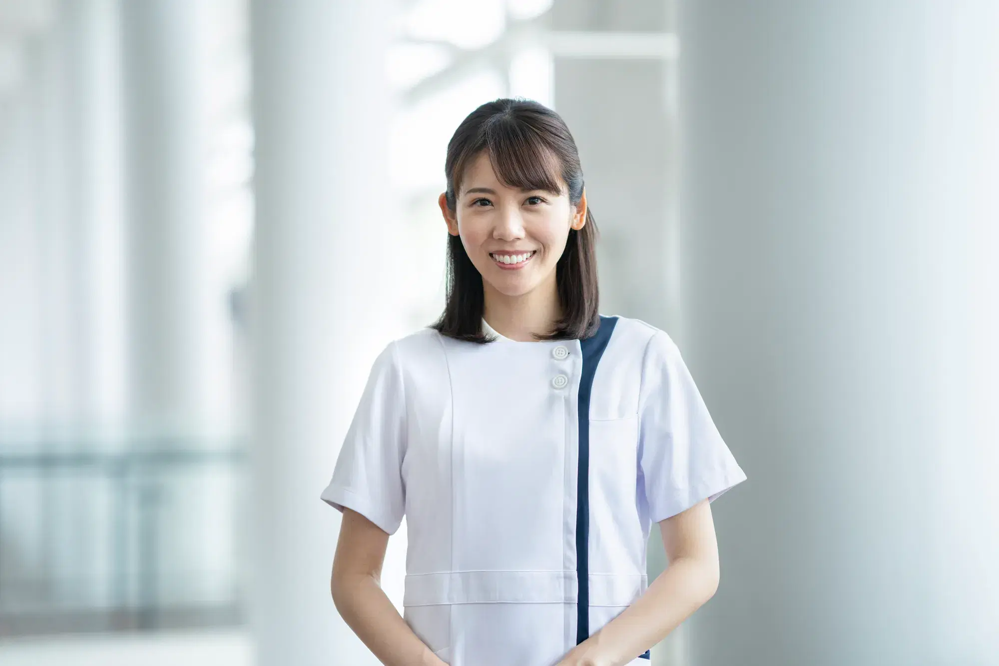 白い服を着た女性の医療従事者が正面を向いて立っている。