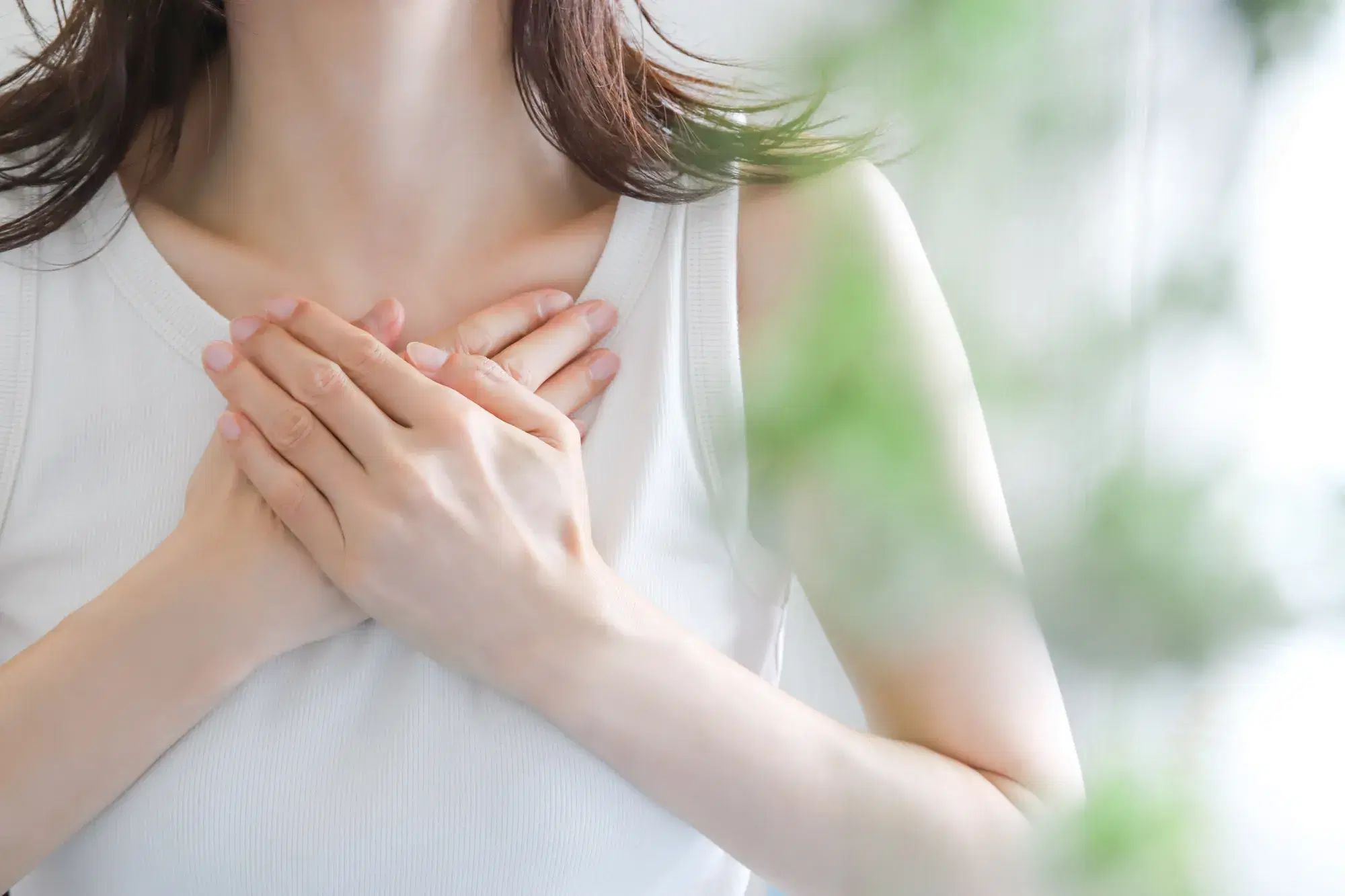 白いタンクトップを着た女性が胸の上に両手を重ねている。