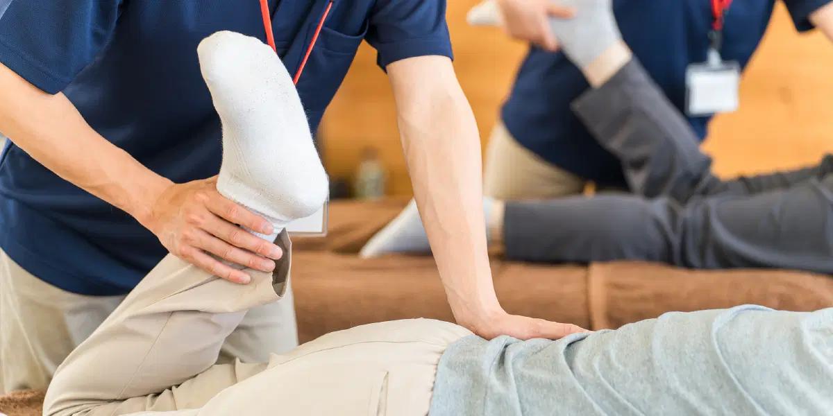 うつ伏せの人の腰を抑えながら、足を曲げマッサージしている