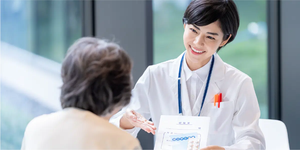 年配の女性に向けて、薬を持ち笑顔で説明をする白衣を着た女性