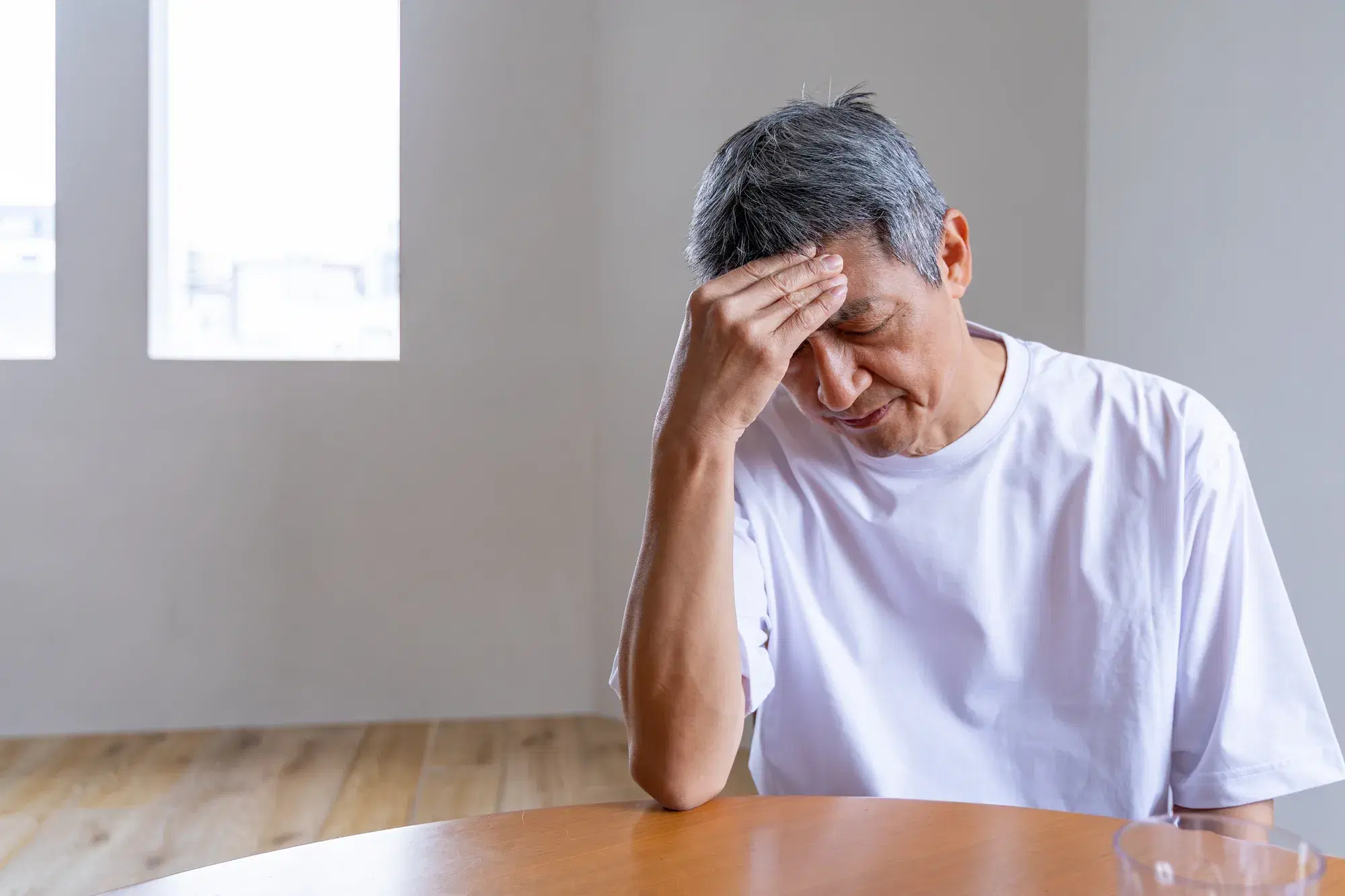 白い服を着た男性が額に手を当てて悩む