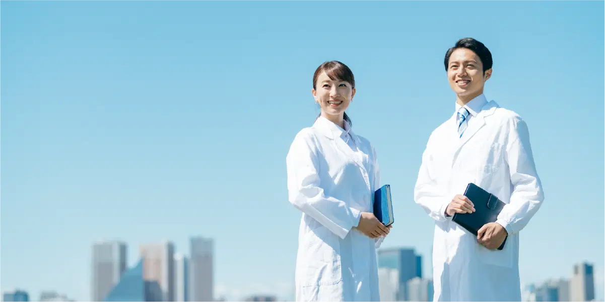 青空の下で白衣を着た男女が二人笑っている
