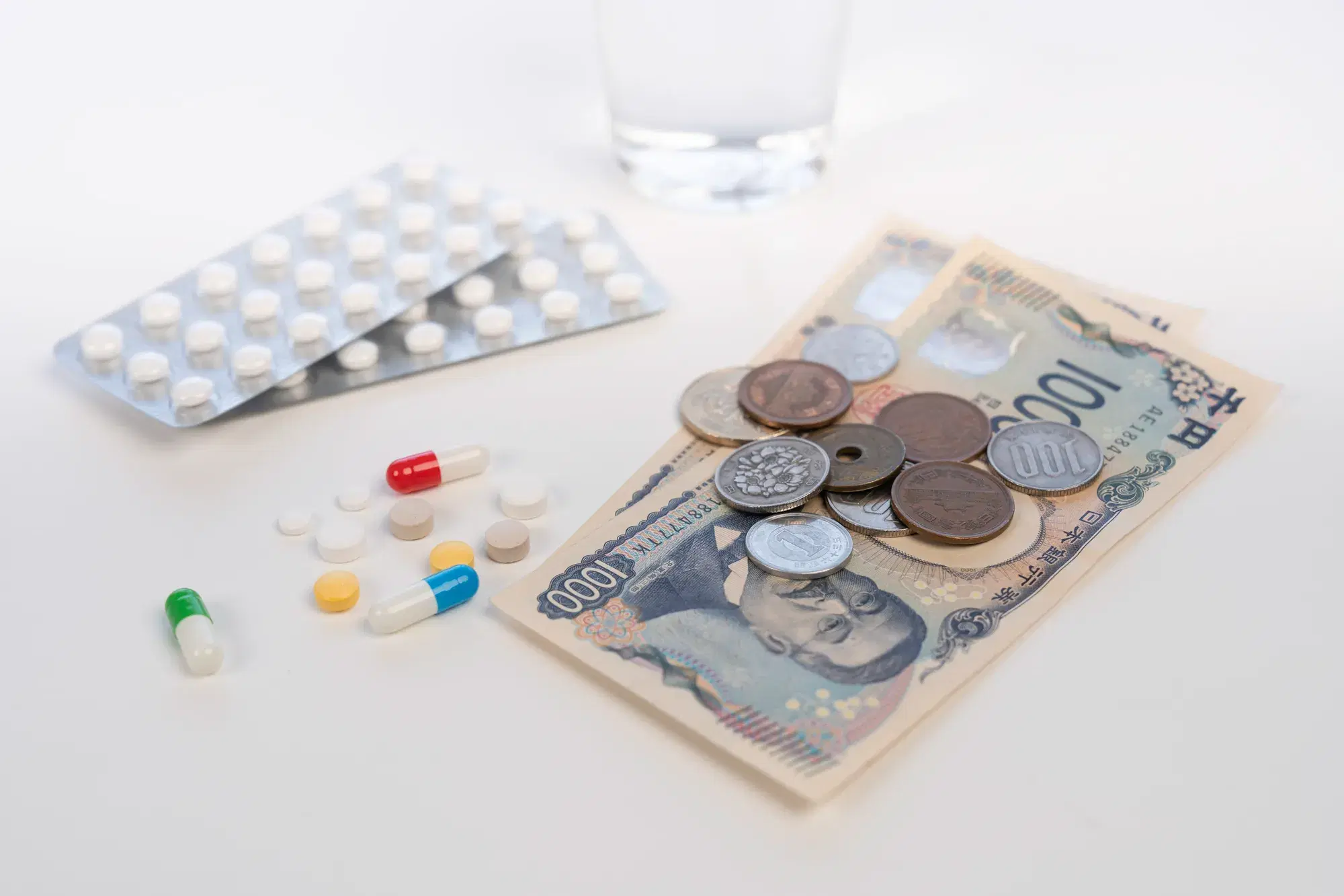 錠剤とガラスコップとお金とカプセル型の薬