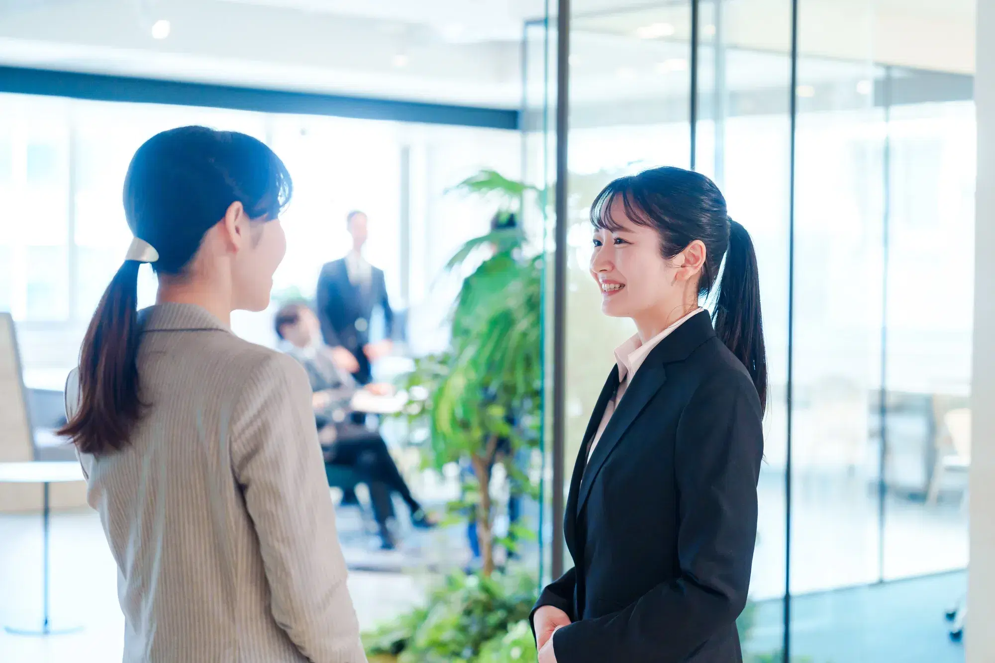 会議室の扉付近でベージュ色のスーツを着た女性が黒いスーツを着た女性と会話
