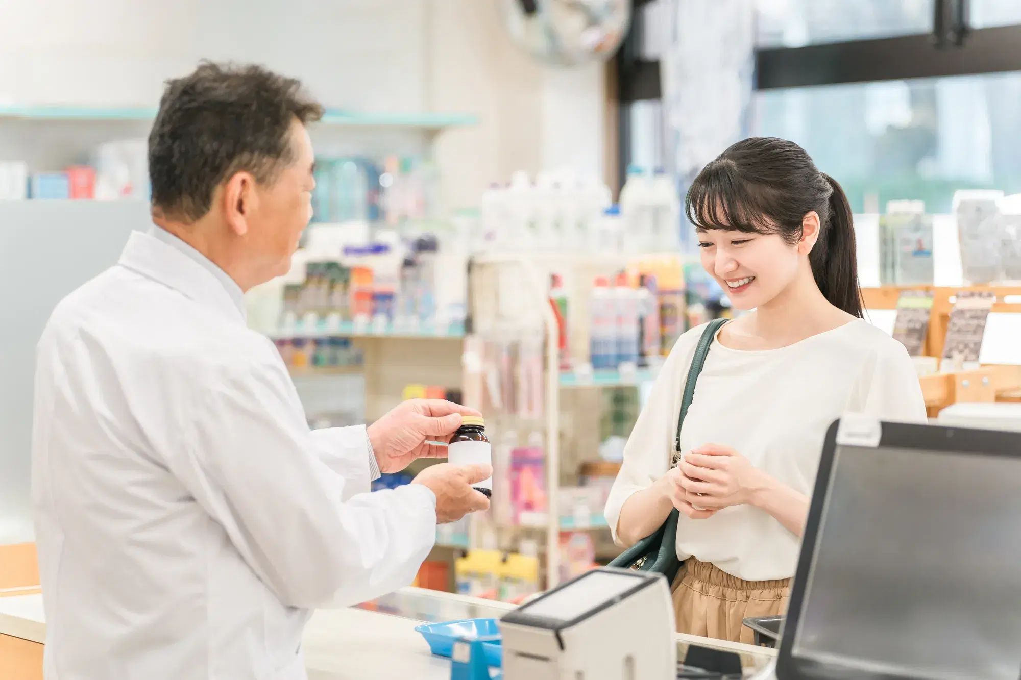白い服に茶色のスカートを着た女性が男性の薬剤師の説明を受けている