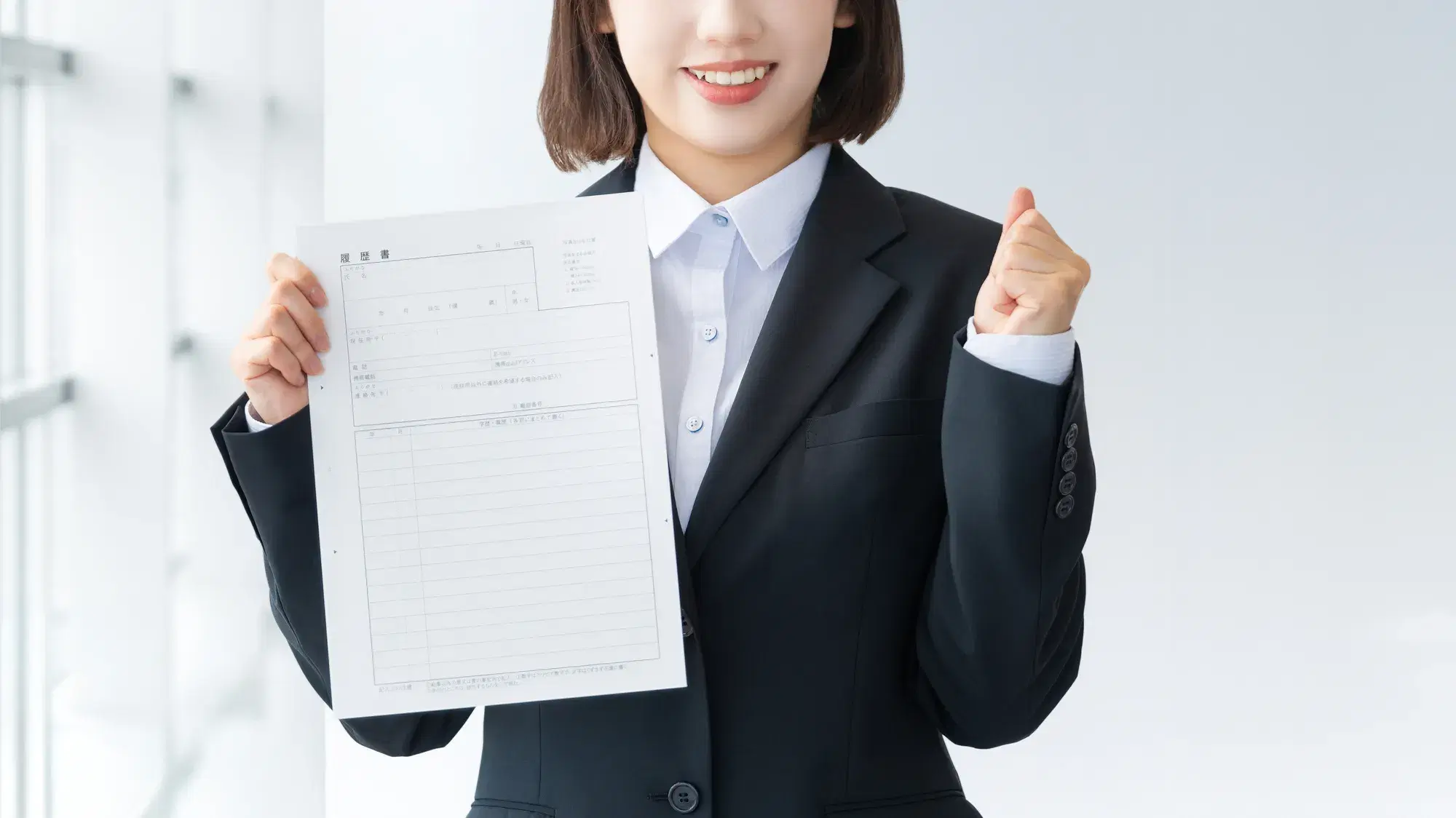 リクルートスーツを着た女性が履歴書を持っている。