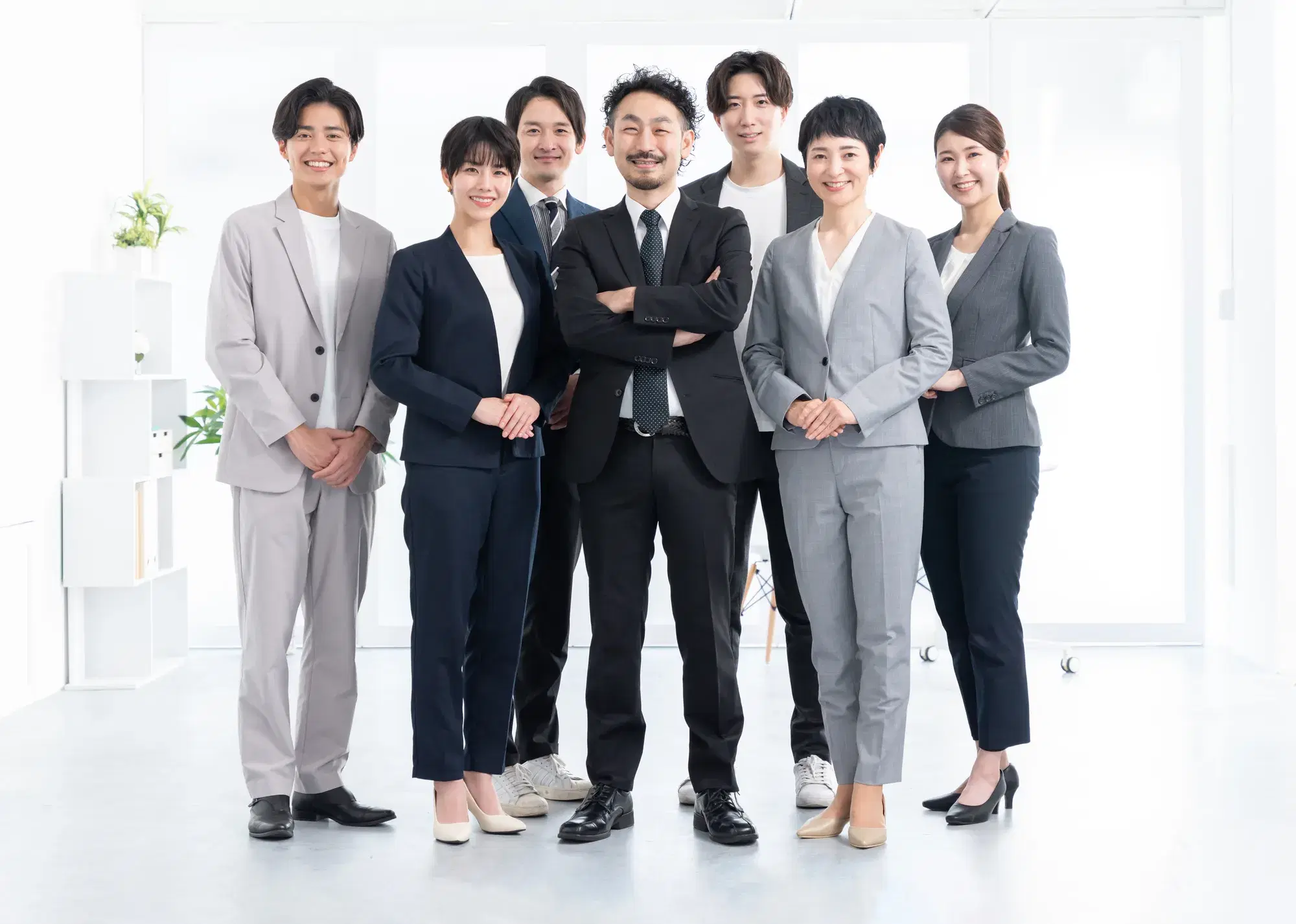 白い空間で7人のスーツを着た社員が集合写真を撮っている