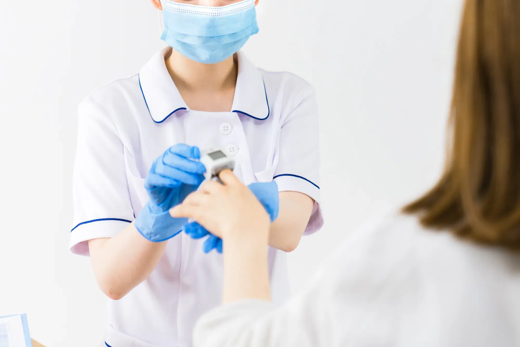 青いマスクに白い白衣の医療従事者の女性が患者に指を使った機械を差し出している